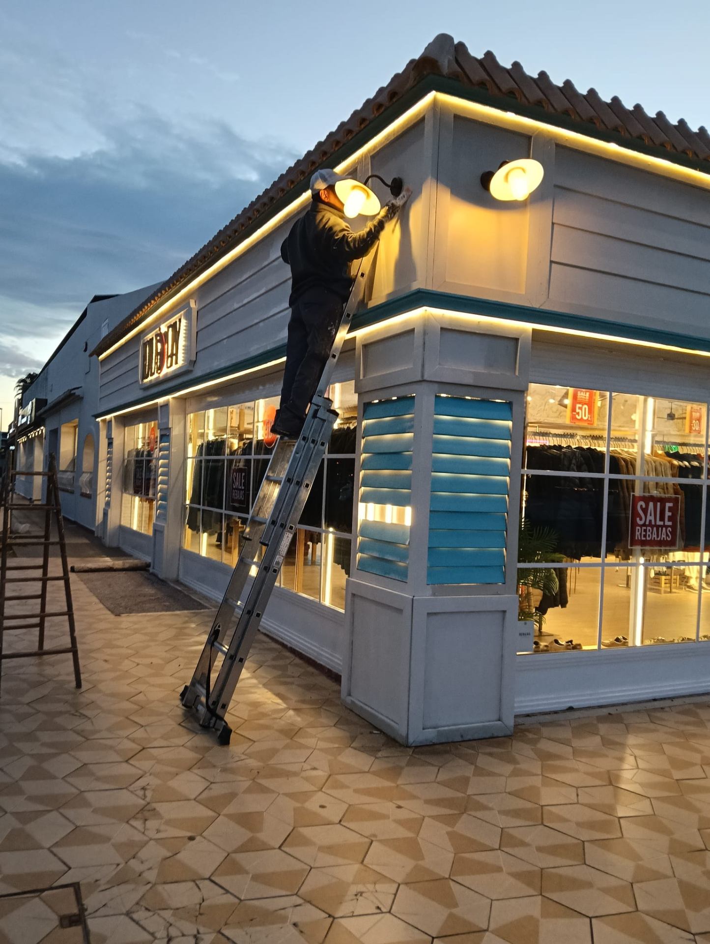 Operario de Mercurius realizando mantenimiento y pintura en fachada de tienda Koala Bay al atardecer